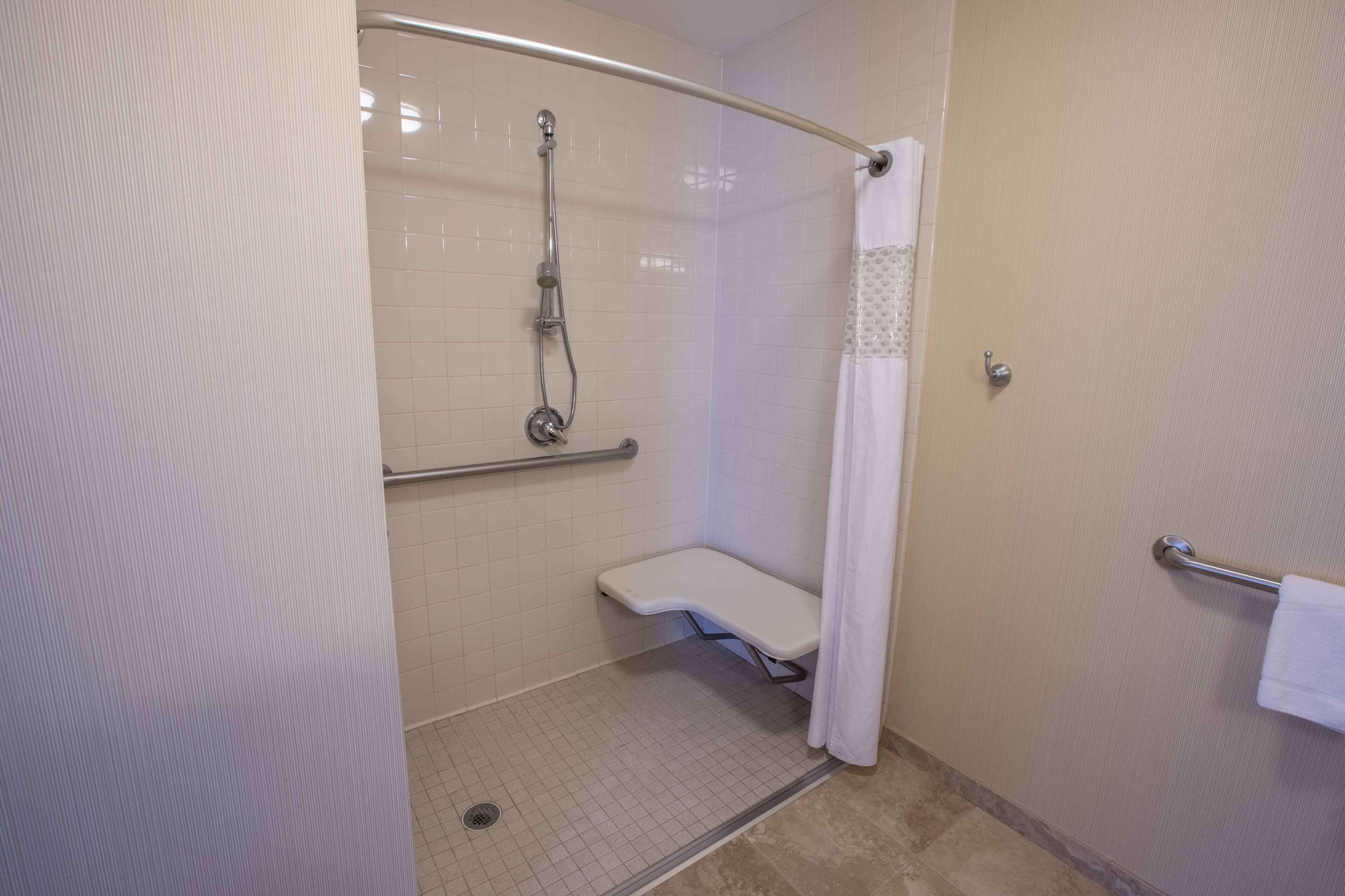 A shower area with a glass door, a handheld showerhead, a grab bar, and a white towel rack.