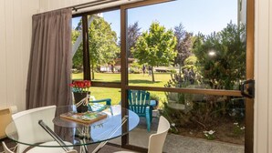A room with a glass table and chairs, a view of a garden, and a window with curtains. - ASURE Explorer Motel & Apartments (Te Anau)