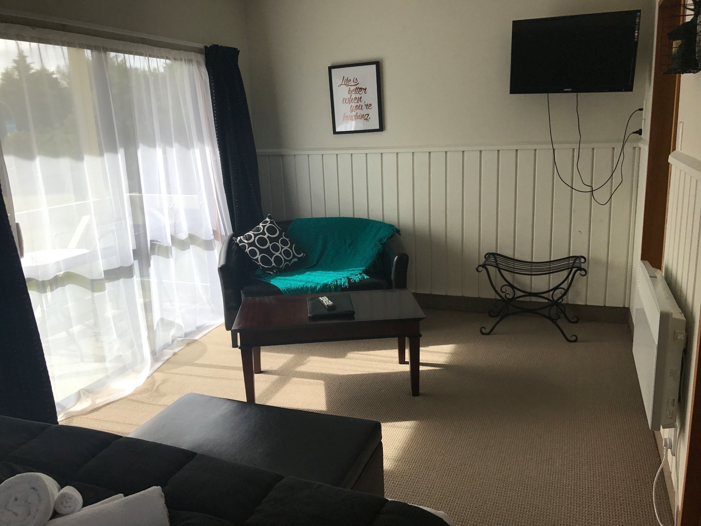 A living room with a sofa, a coffee table, a TV mounted on the wall, and a window with curtains.