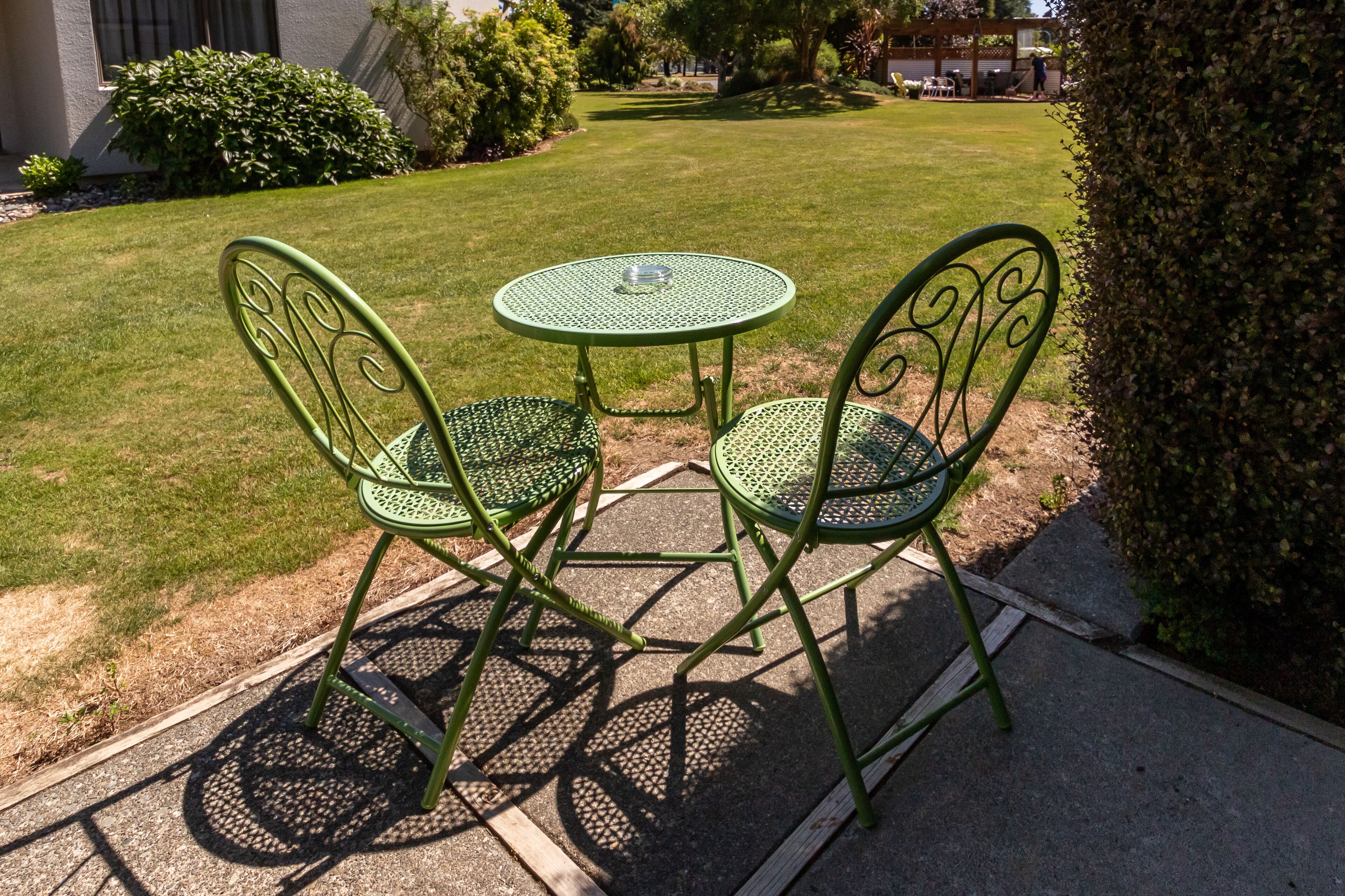 A small outdoor seating area with a round table and two chairs, surrounded by a well-maintained lawn and a hedge.