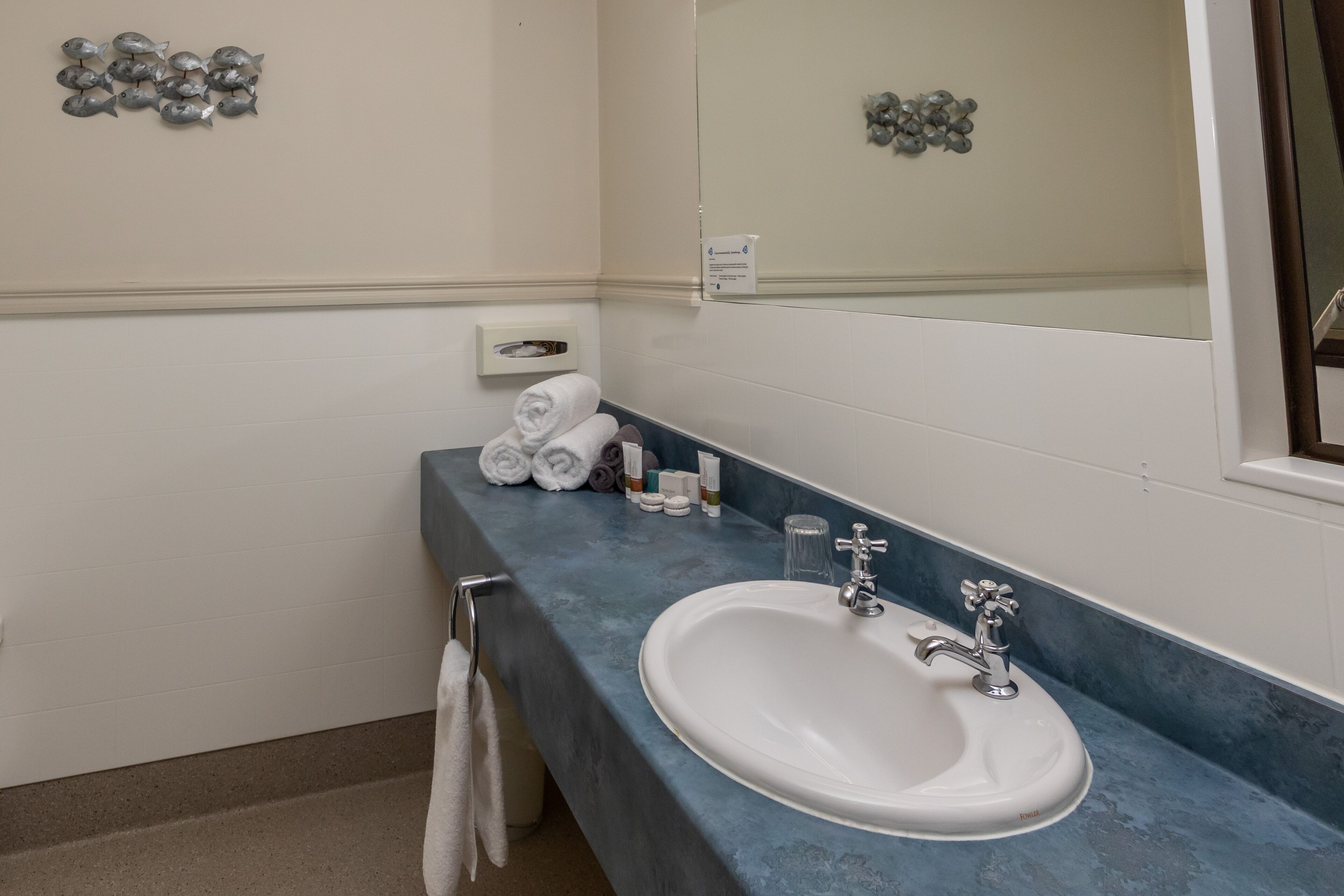 A bathroom with a white sink, blue countertop, and a mirror. There are towels and toiletries on the counter.