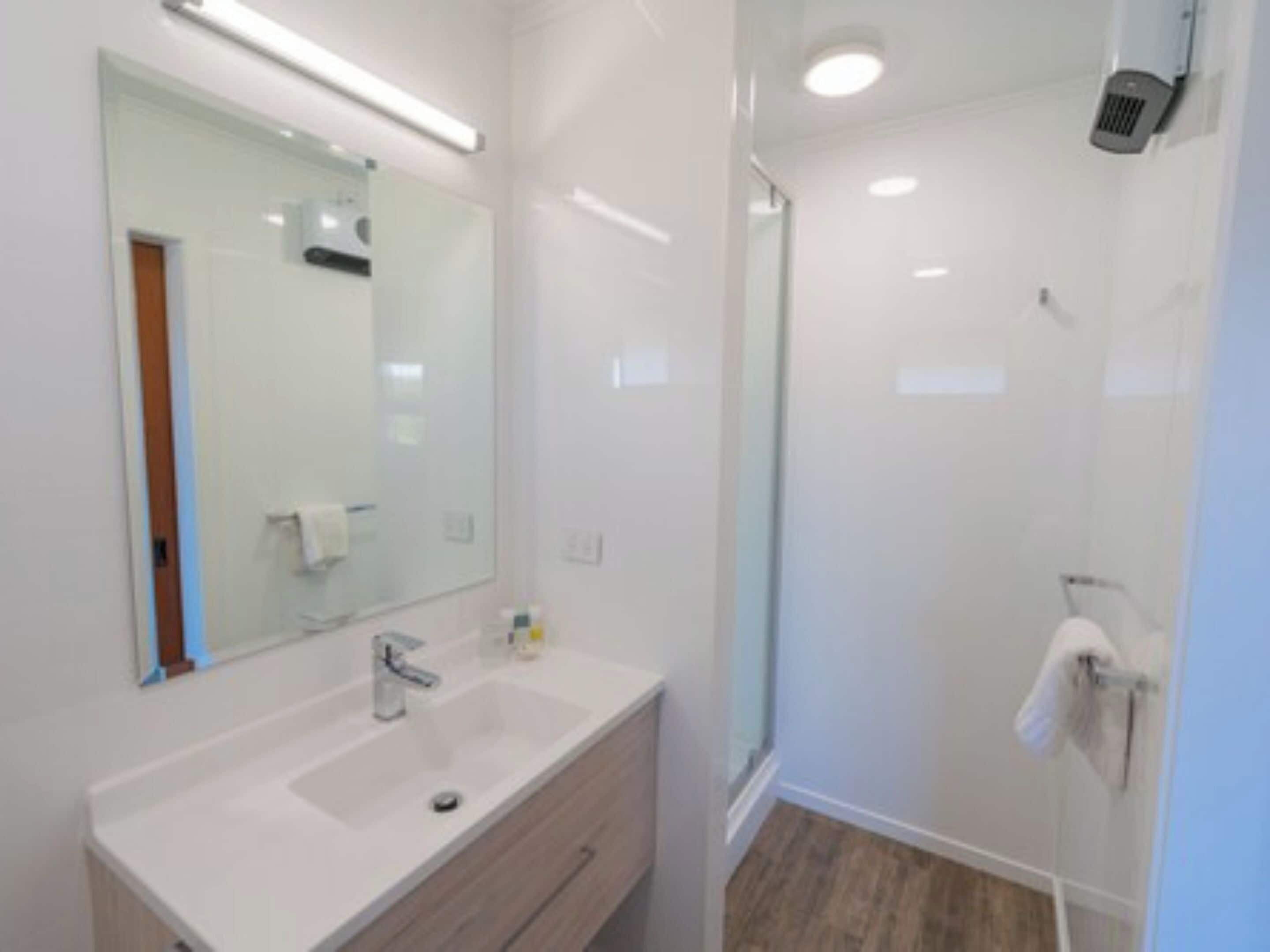 A modern bathroom with a white sink, mirror, and shower.