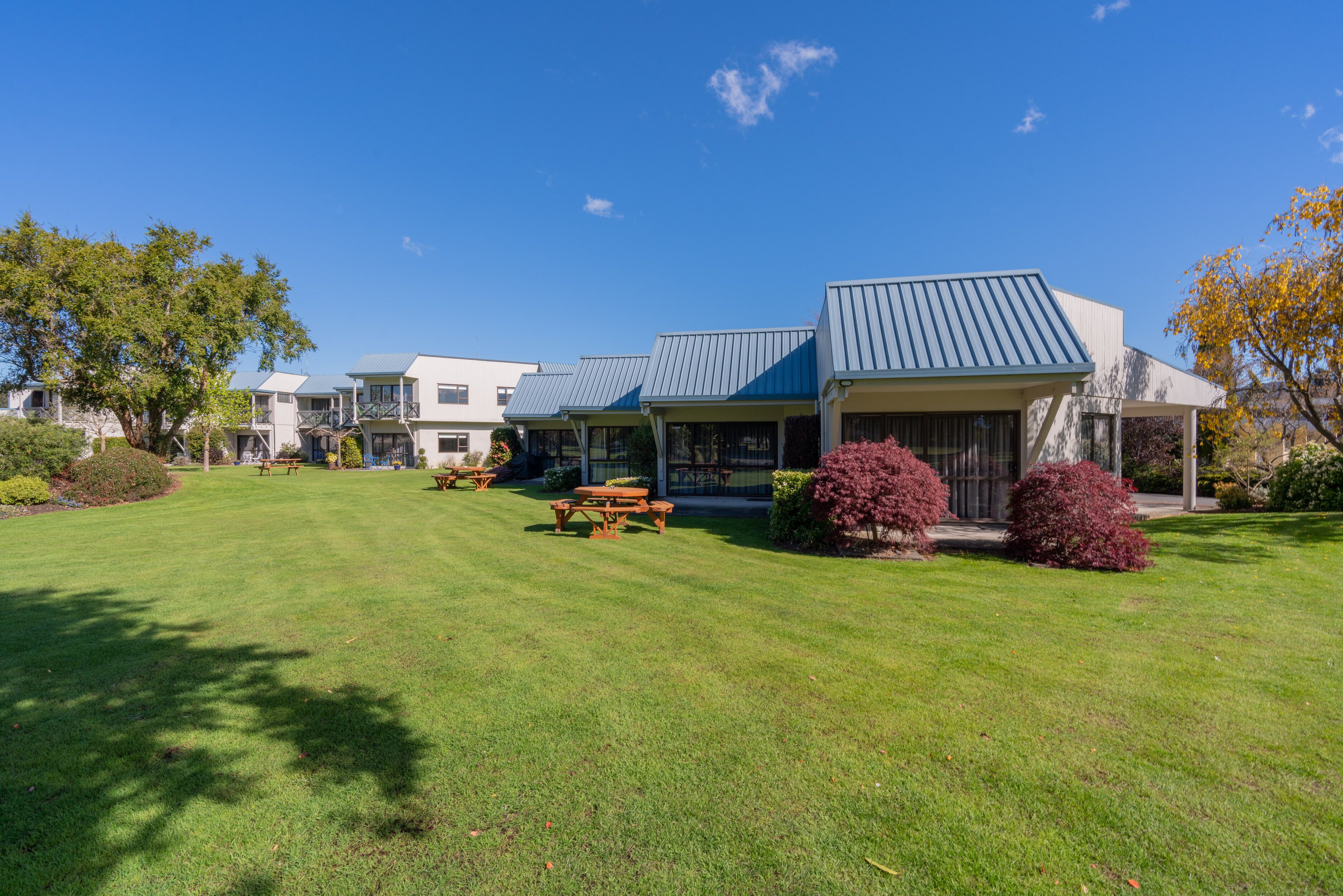 A row of modern buildings with flat roofs and covered patios, surrounded by well-maintained lawns and picnic tables.