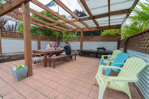 An outdoor patio with wooden tables and chairs, a pergola, and a view of the surrounding greenery. - ASURE Explorer Motel & Apartments (Te Anau)