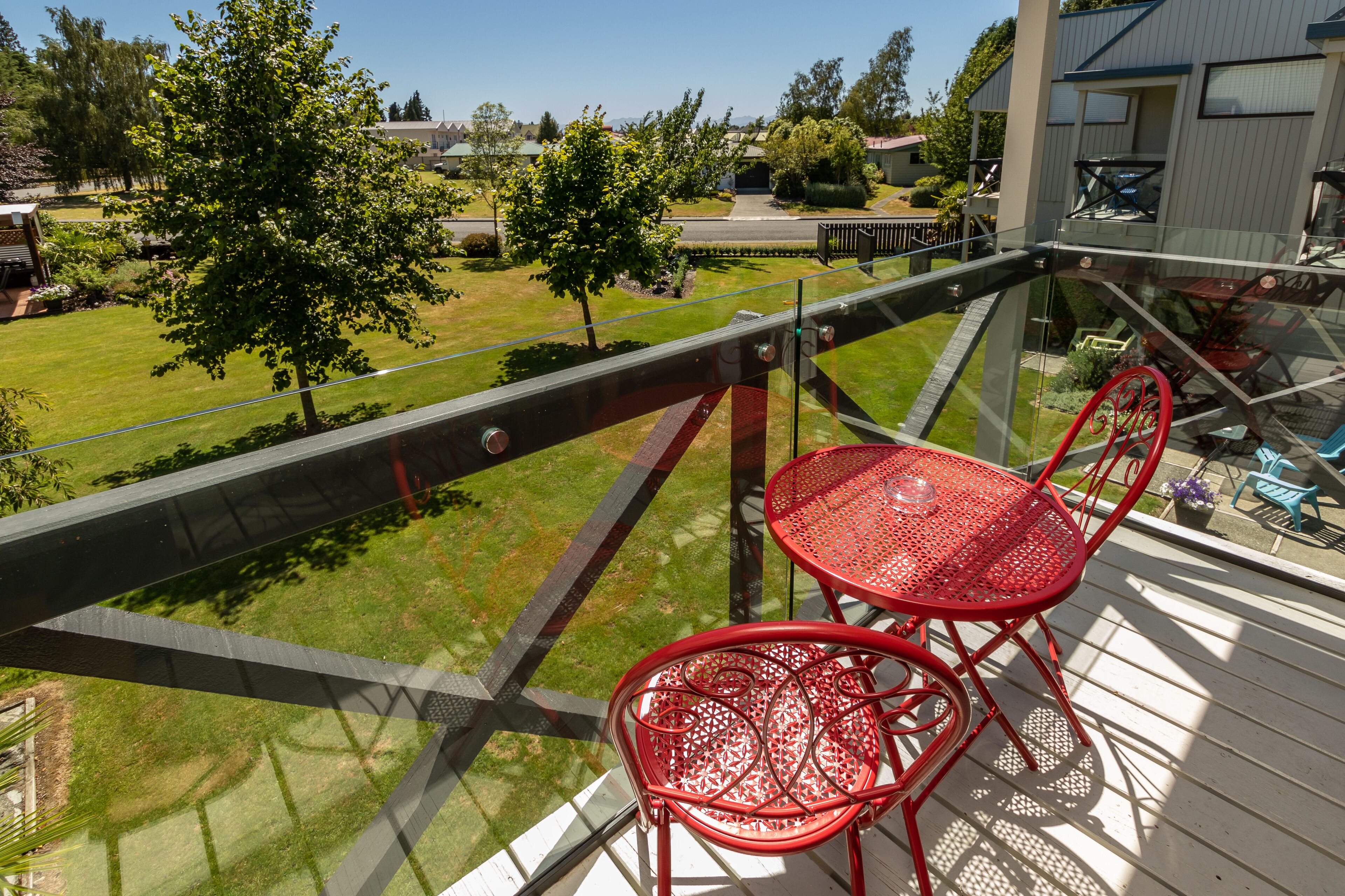 A balcony with a glass railing overlooking a well-maintained lawn and residential area.