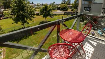 A balcony with a glass railing overlooking a well-maintained lawn and residential area.