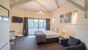 A bedroom with a bed, a desk, a chair, a sofa, a TV, and a painting on the wall. - ASURE Explorer Motel & Apartments (Te Anau)