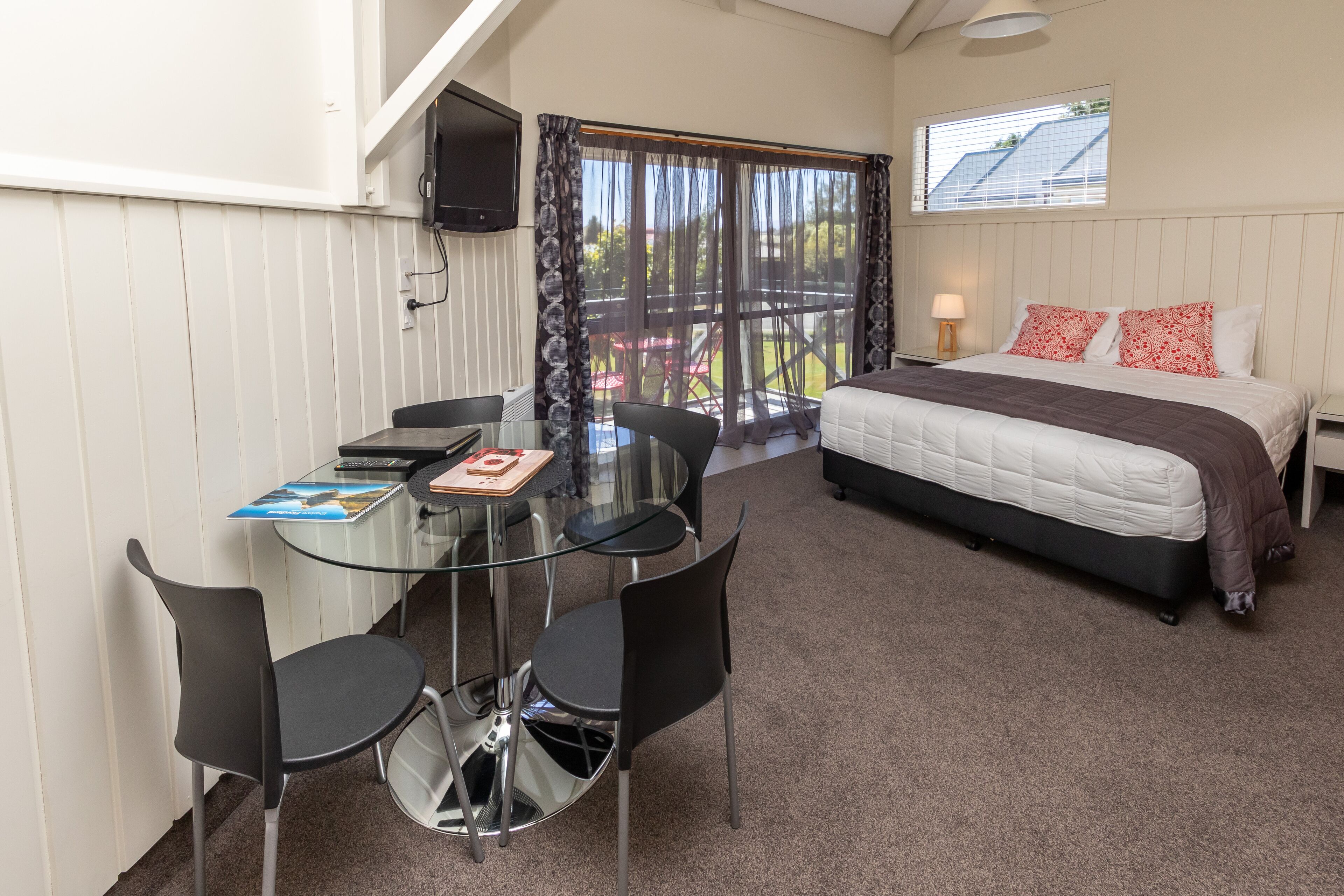 A bedroom with a bed, a TV, and a balcony with chairs.