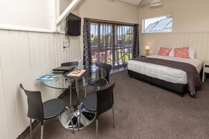 A bedroom with a bed, a TV, and a balcony with chairs.