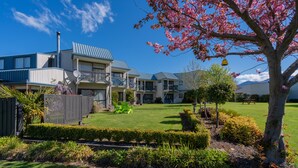 A multi-story hotel with a blue roof, a well-maintained lawn, and a variety of plants and shrubs. - ASURE Explorer Motel & Apartments (Te Anau)