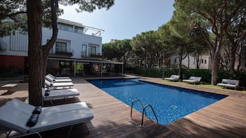 Una piscina al aire libre, sombrillas, sillones reclinables de piscina