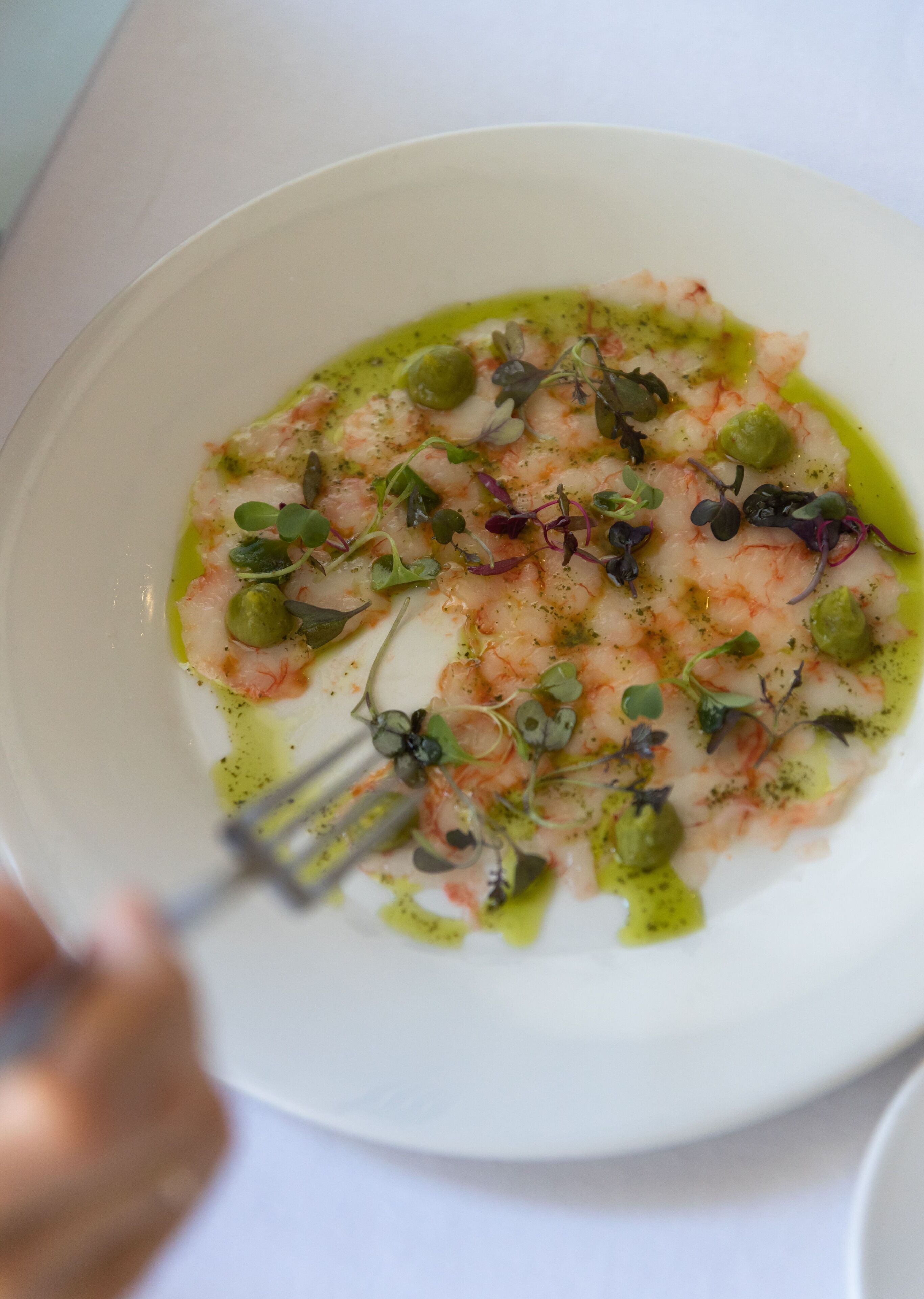 Une assiette blanche contenant un plat de fruits de mer, agrémenté de verdure et d’une sauce verte, et une fourchette à côté.