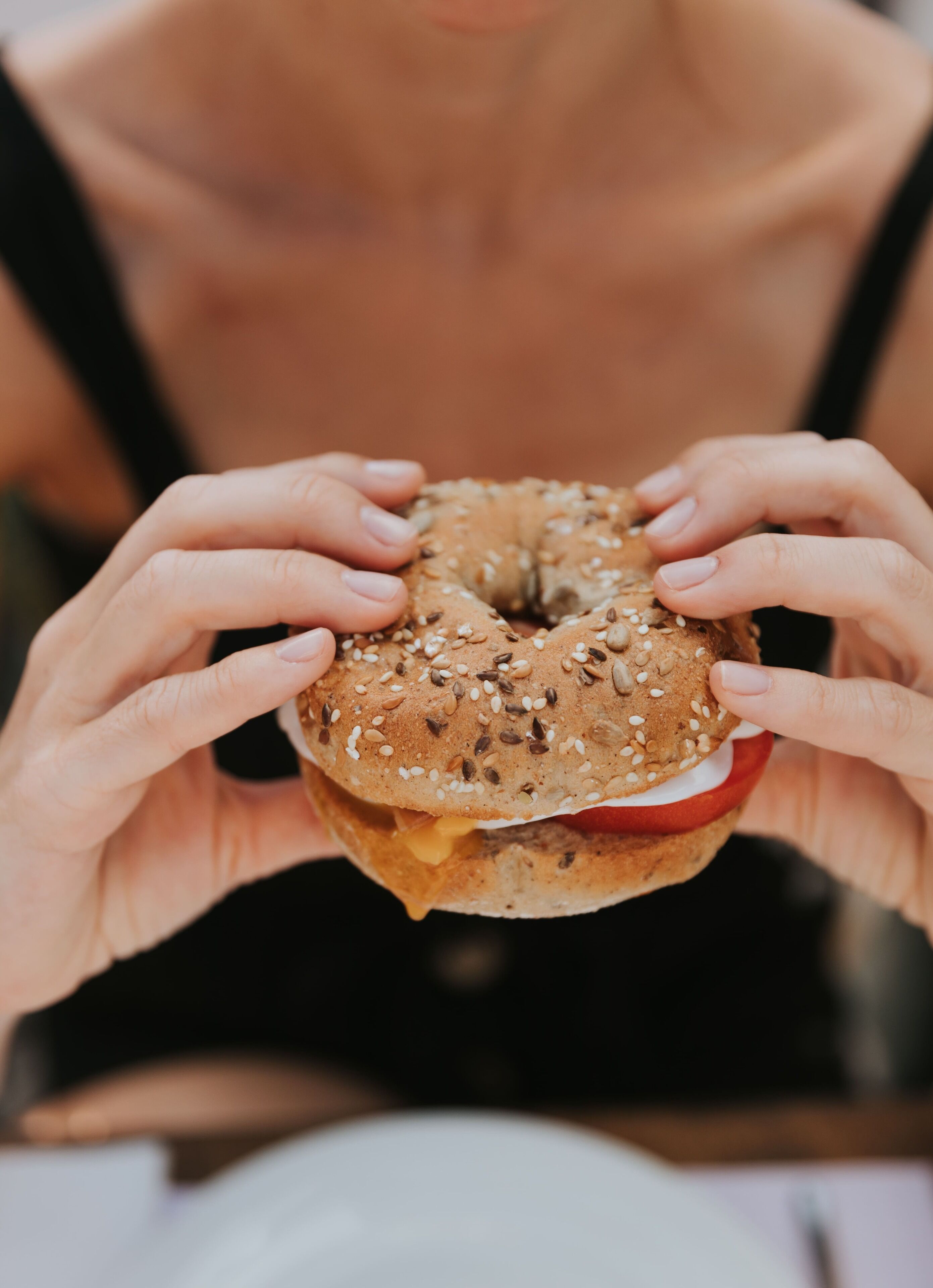 Una persona sosteniendo un sándwich de bagel con semillas visibles y una rodaja de tomate.