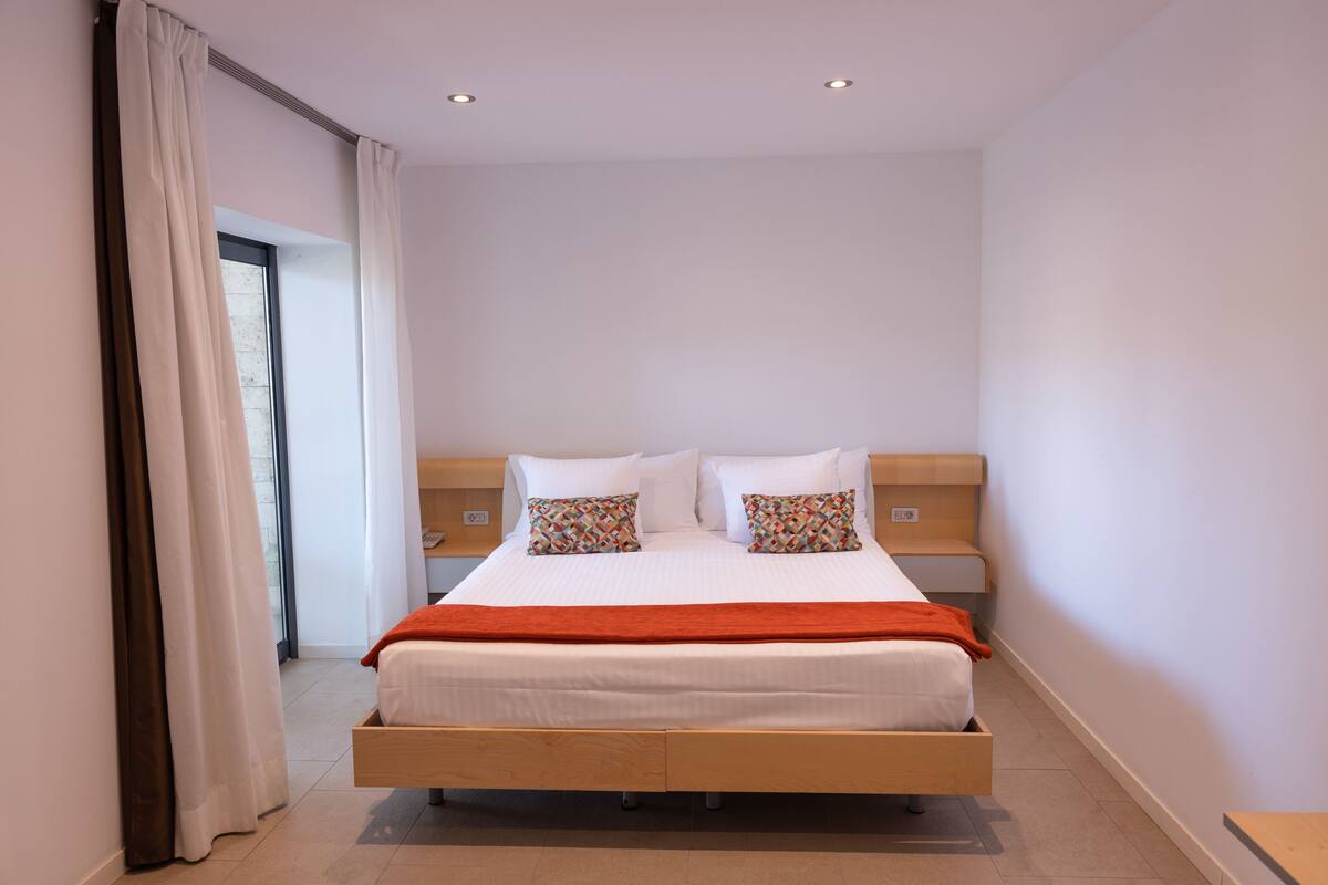 A modern bedroom with a wooden bed, white bedding, and patterned pillows.