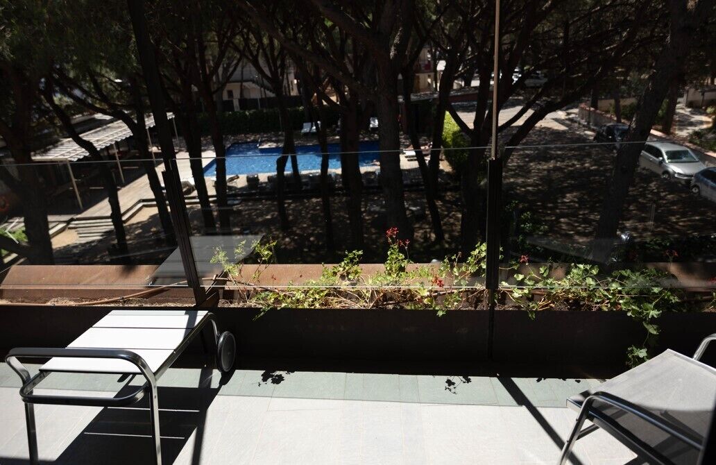 A balcony with a view of a swimming pool, surrounded by trees and parked cars.