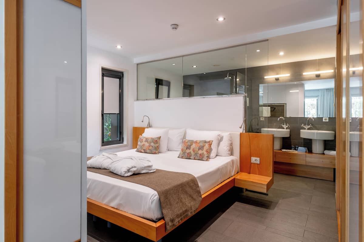 A modern bedroom with a large bed, bedside tables, a mirror, and a bathroom with a sink and mirror.