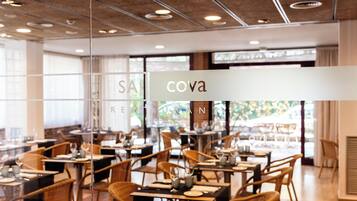Ein Restaurant mit Tischen, Stühlen und einer Glastrennwand, mit einem Schild, auf dem 'cova' steht.