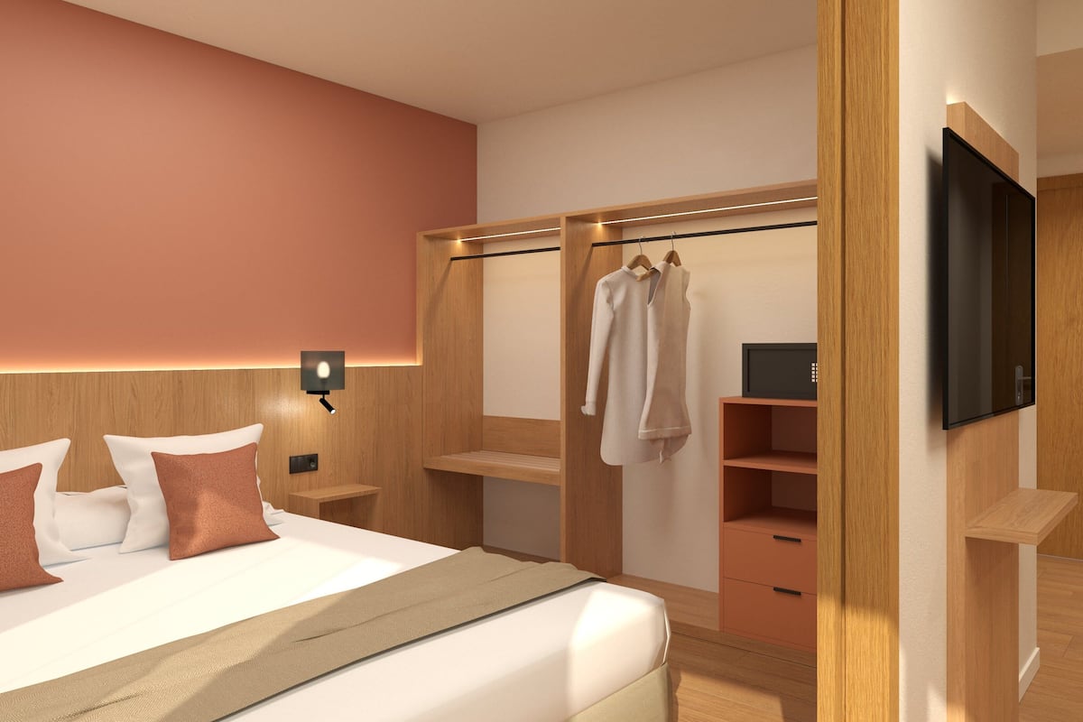 A modern hotel room with a large bed, a wooden wardrobe, a flat-screen TV, and a bedside table.