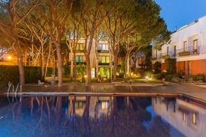 A swimming pool surrounded by trees and a building with multiple balconies. - Hotel NM Suites by Escampa Hotels (Castell-Platja d'Aro)