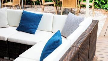 A white sofa with blue and patterned cushions, a wicker bench, and a wooden deck.