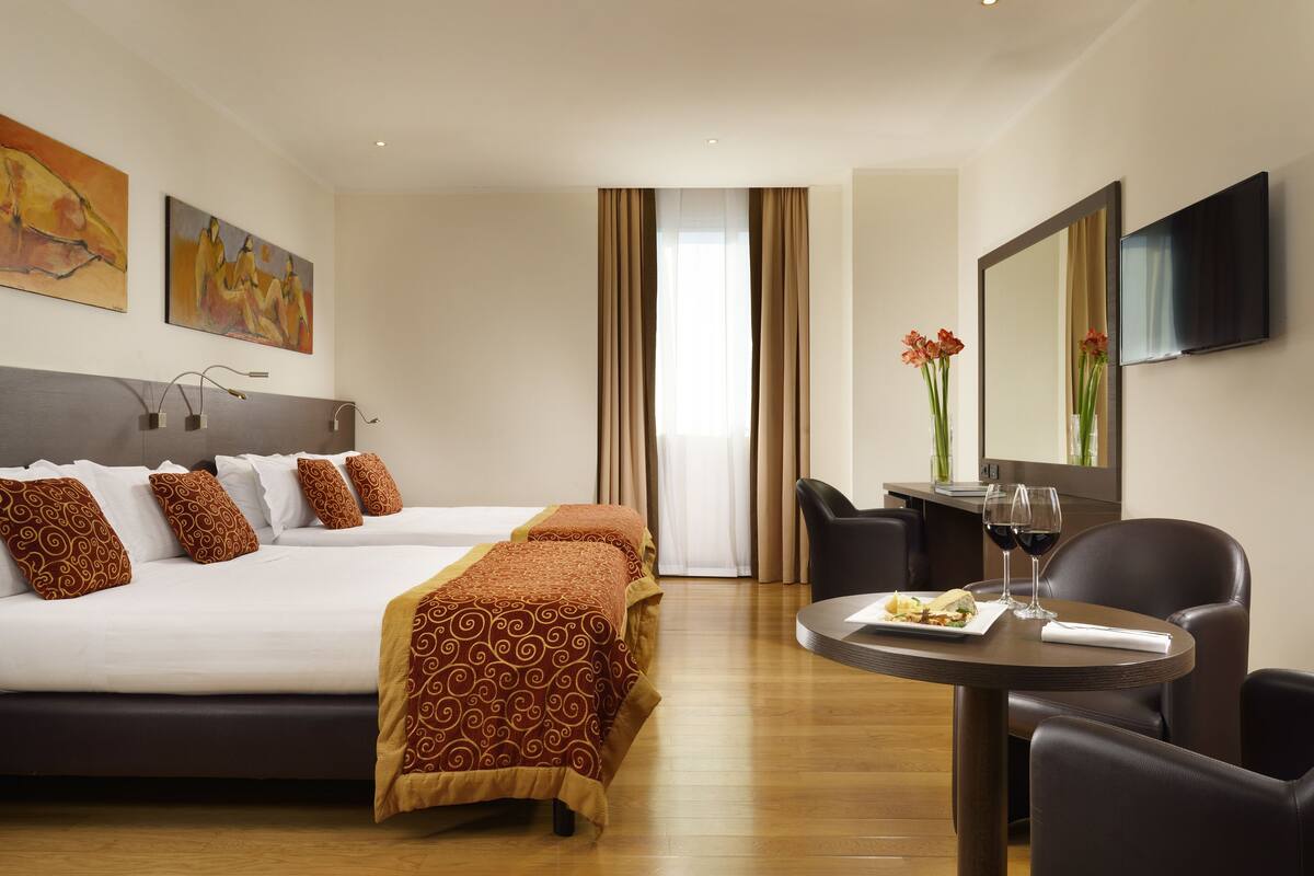 A hotel room with a large bed, a dining table with chairs, and artwork on the walls.