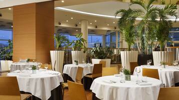 Un restaurante con mesas redondas, manteles blancos y sillas de madera.