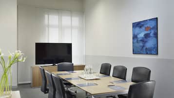 Ein Konferenzraum mit langem Tisch, schwarzen Stühlen, einem Fernseher und einem Gemälde an der Wand.