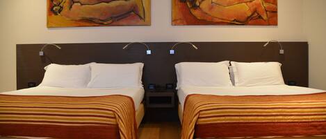A hotel room with two beds, each with white linens and striped blankets. There are two paintings on the wall above the beds.