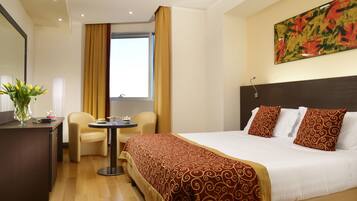 Habitación de hotel con cama, escritorio, silla, una mesita y ventana con cortinas.