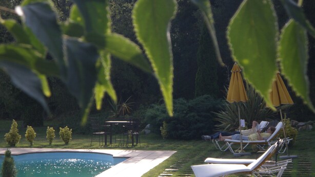 A swimming pool with lounge chairs and umbrellas, surrounded by greenery. - Hotel Mas Vilalonga Petit (Cassa de la Selva)
