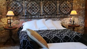 A bed with a patterned bedspread and pillows, two bedside tables with lamps, and a stone wall backdrop. - Hotel Mas Vilalonga Petit (Cassa de la Selva)