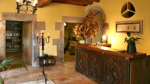 A lobby with a wooden reception desk, a chandelier, a potted plant, and a bookshelf. - Hotel Mas Vilalonga Petit (Cassa de la Selva)