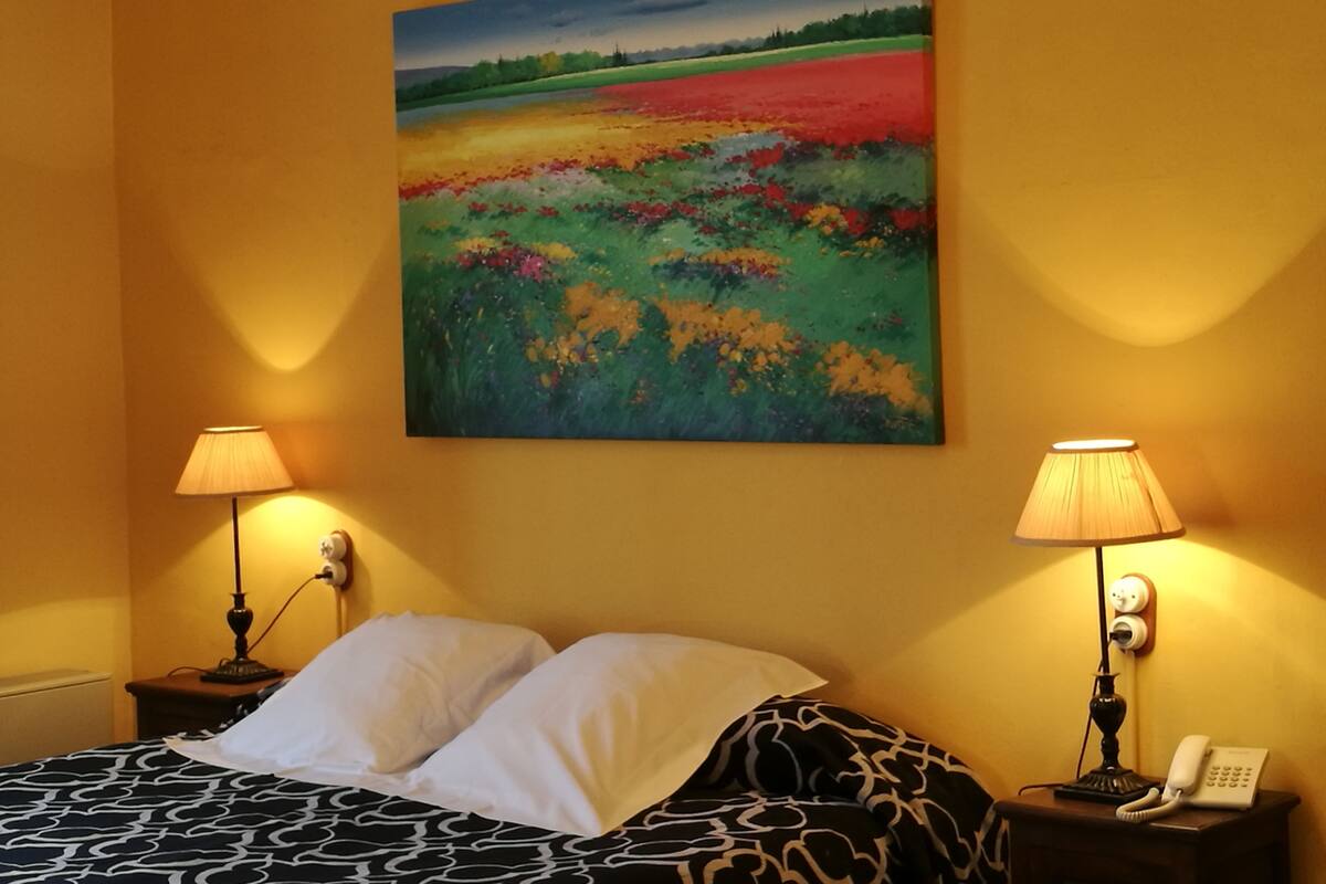 Une chambre d’hôtel avec un lit, deux lampes de chevet, un tableau au mur et un téléphone sur la table de chevet.