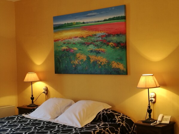 A hotel room with a bed, two bedside lamps, a painting on the wall, and a telephone on the nightstand.