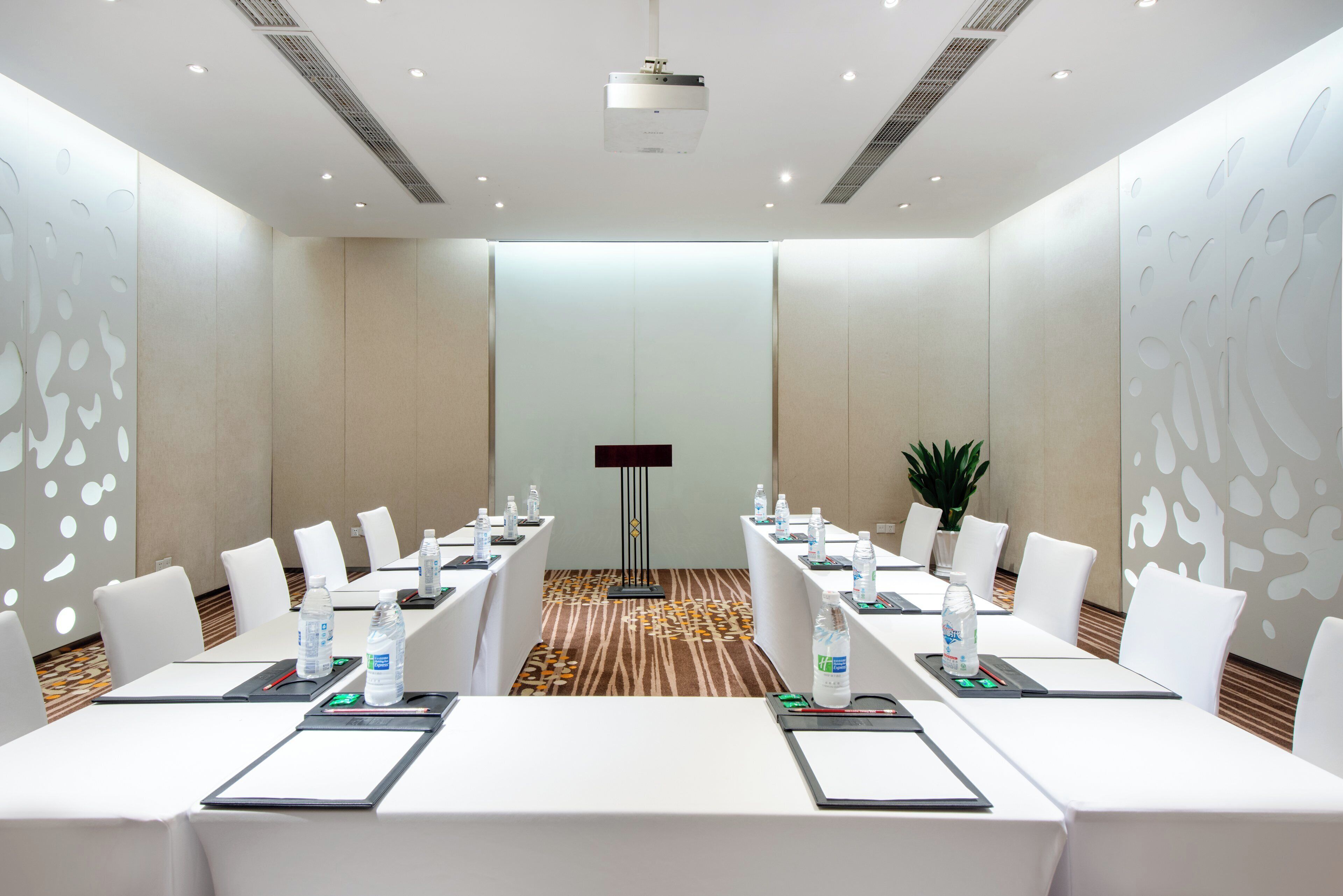 A conference room with white tables, chairs, and a projector screen.