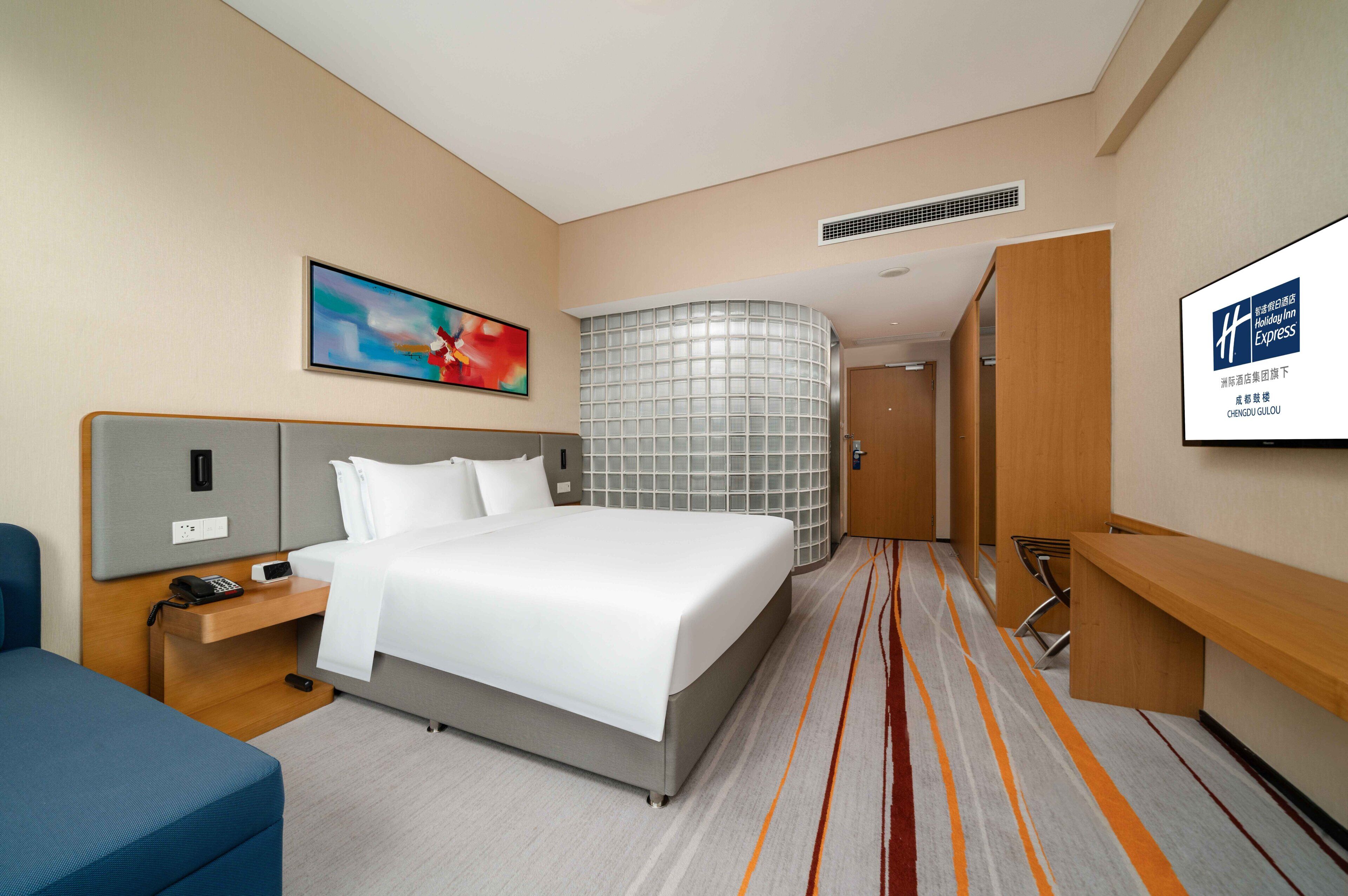 Une chambre d’hôtel comprenant un lit, une table de chevet, un bureau, une chaise, une télévision et une salle de bain avec douche.