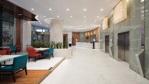 Um hall amplo com balcão de recepção, área de estar e um elevador moderno.