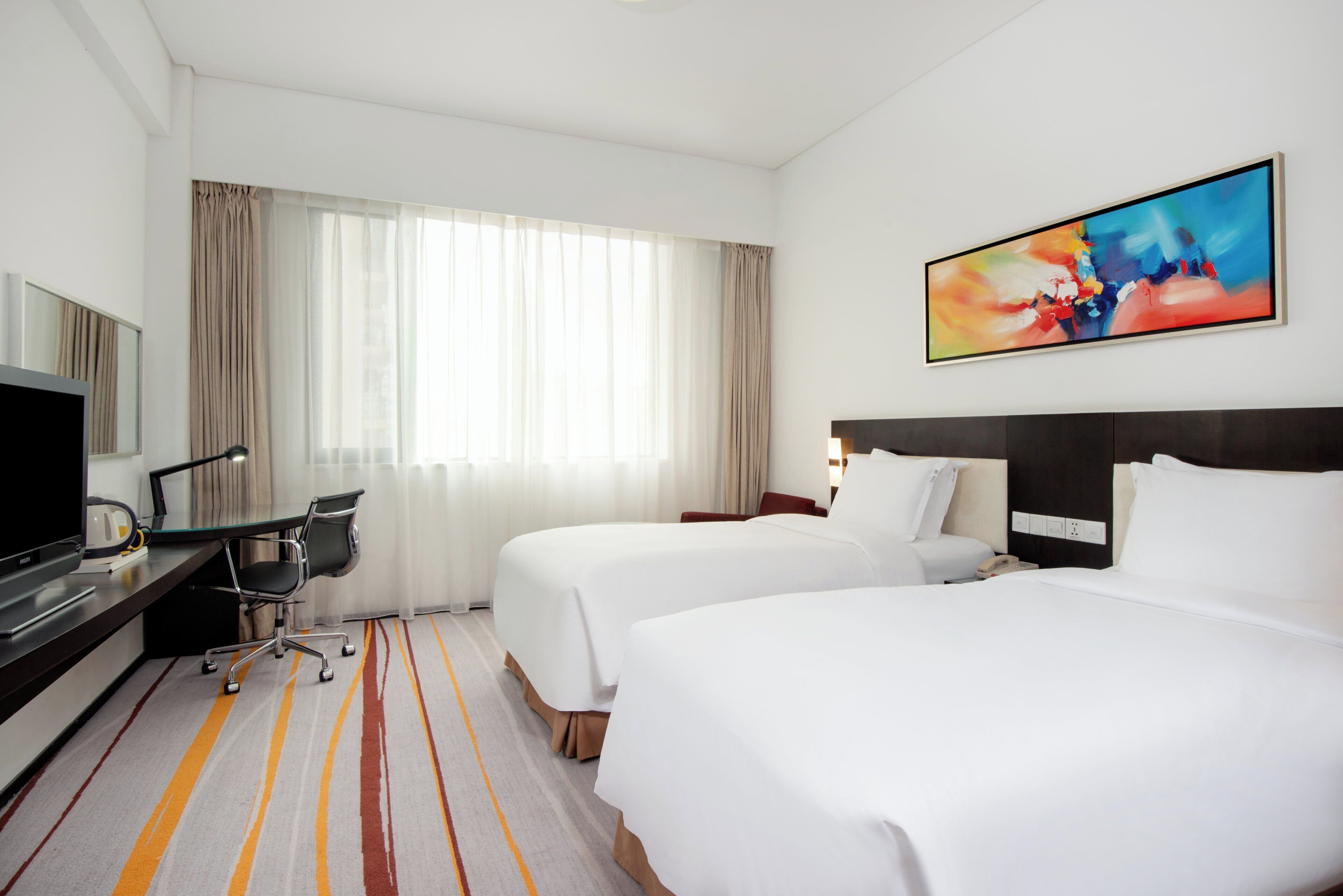 Een hotelkamer met twee bedden, een bureau met stoel, een televisie en een schilderij aan de muur.