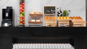 Um buffet de café da manhã com frutas, pães, doces e uma máquina de café.