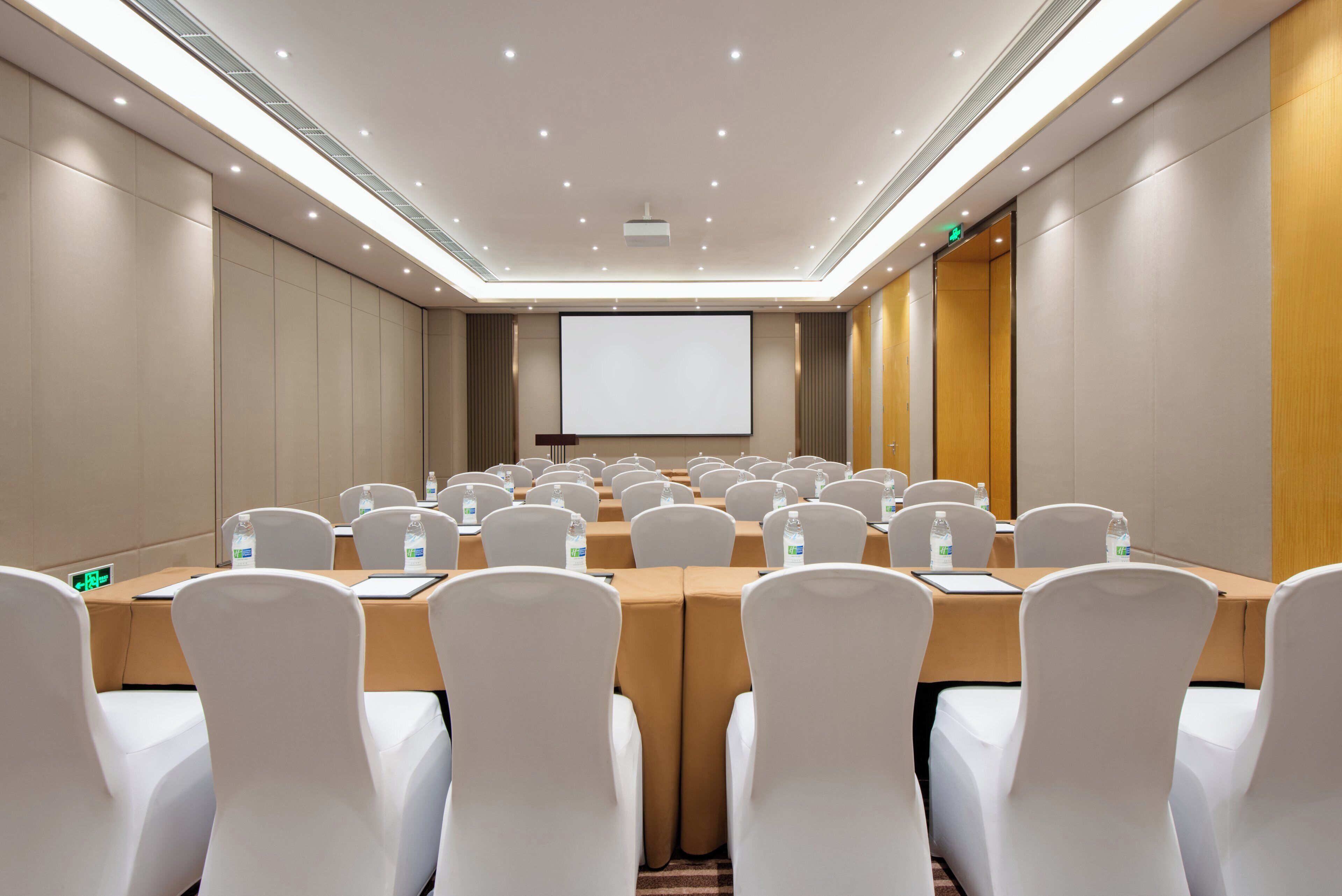 A conference room with a long table, white chairs, and a projector screen.