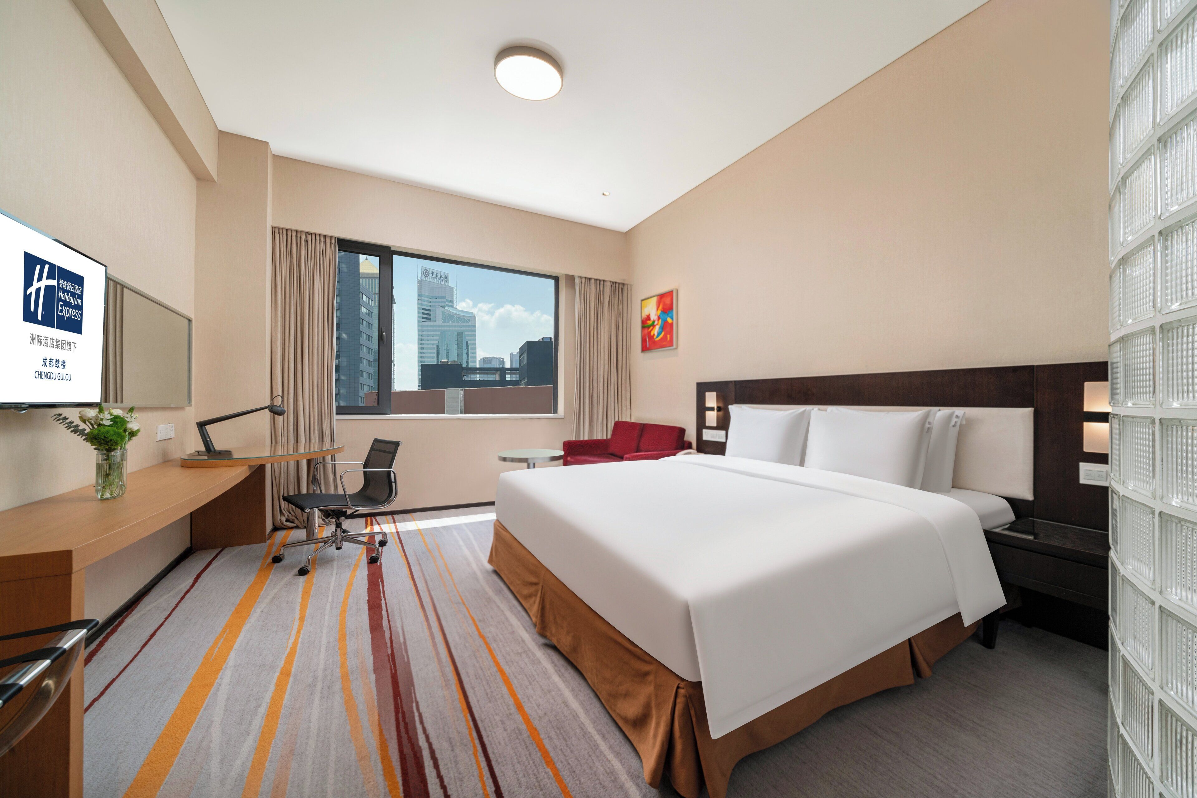 A hotel room with a large bed, a desk with a chair, a television, and a window with curtains.