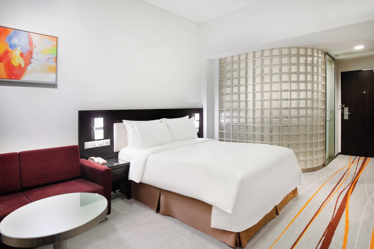 Una habitación de hotel con una cama, un sofá rojo, una mesita y un panel decorativo en la pared.