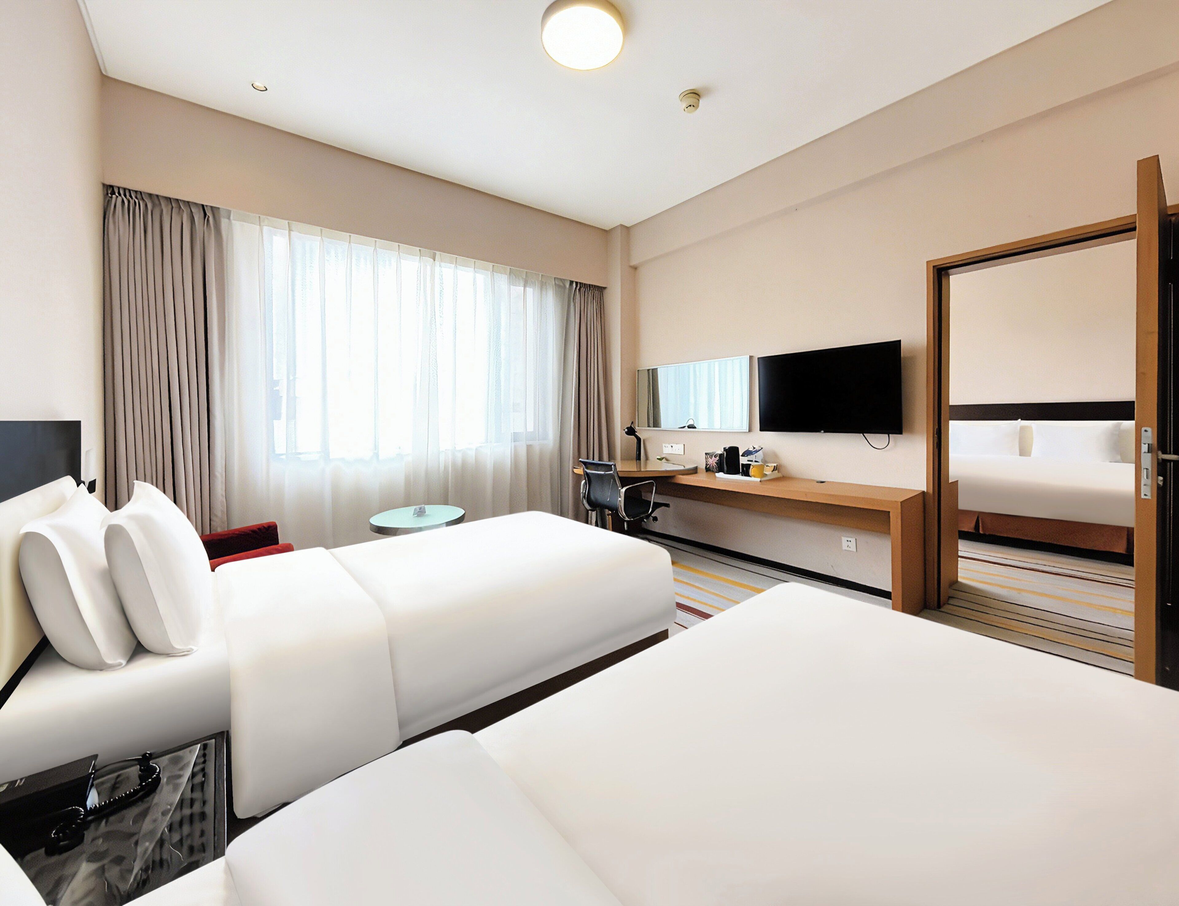 A hotel room with a bed, a desk, a chair, a television, and a window with curtains.