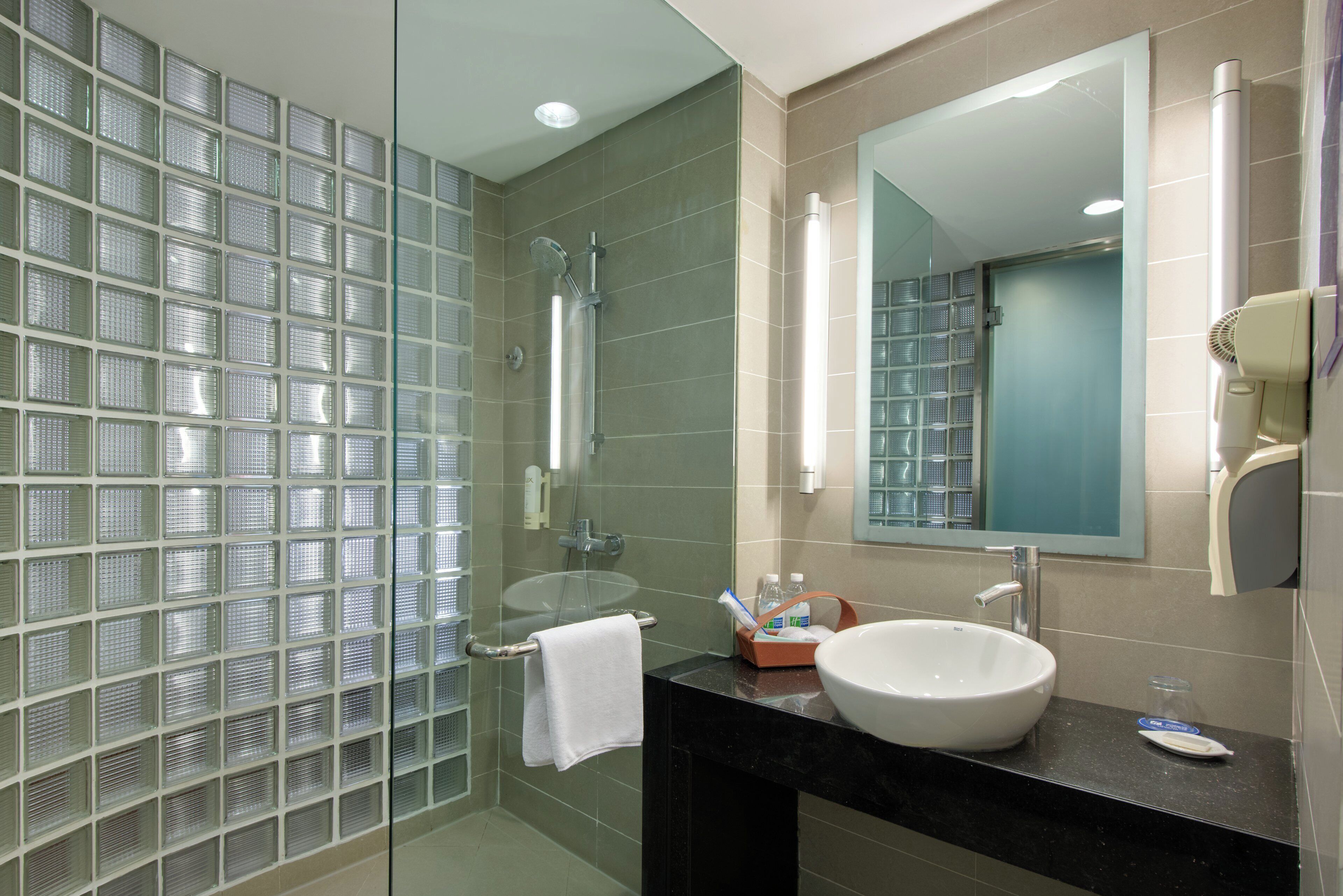 A modern bathroom with a glass shower enclosure, a white sink, and a large mirror.