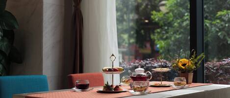 Una mesa servida con té, pasteles y una presentación de frutas en una habitación con vistas a la vegetación.