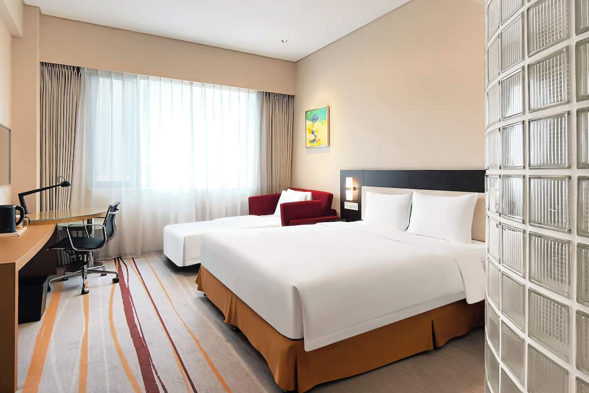 A hotel room with a large bed, a desk with a chair, a computer, and a window with curtains.