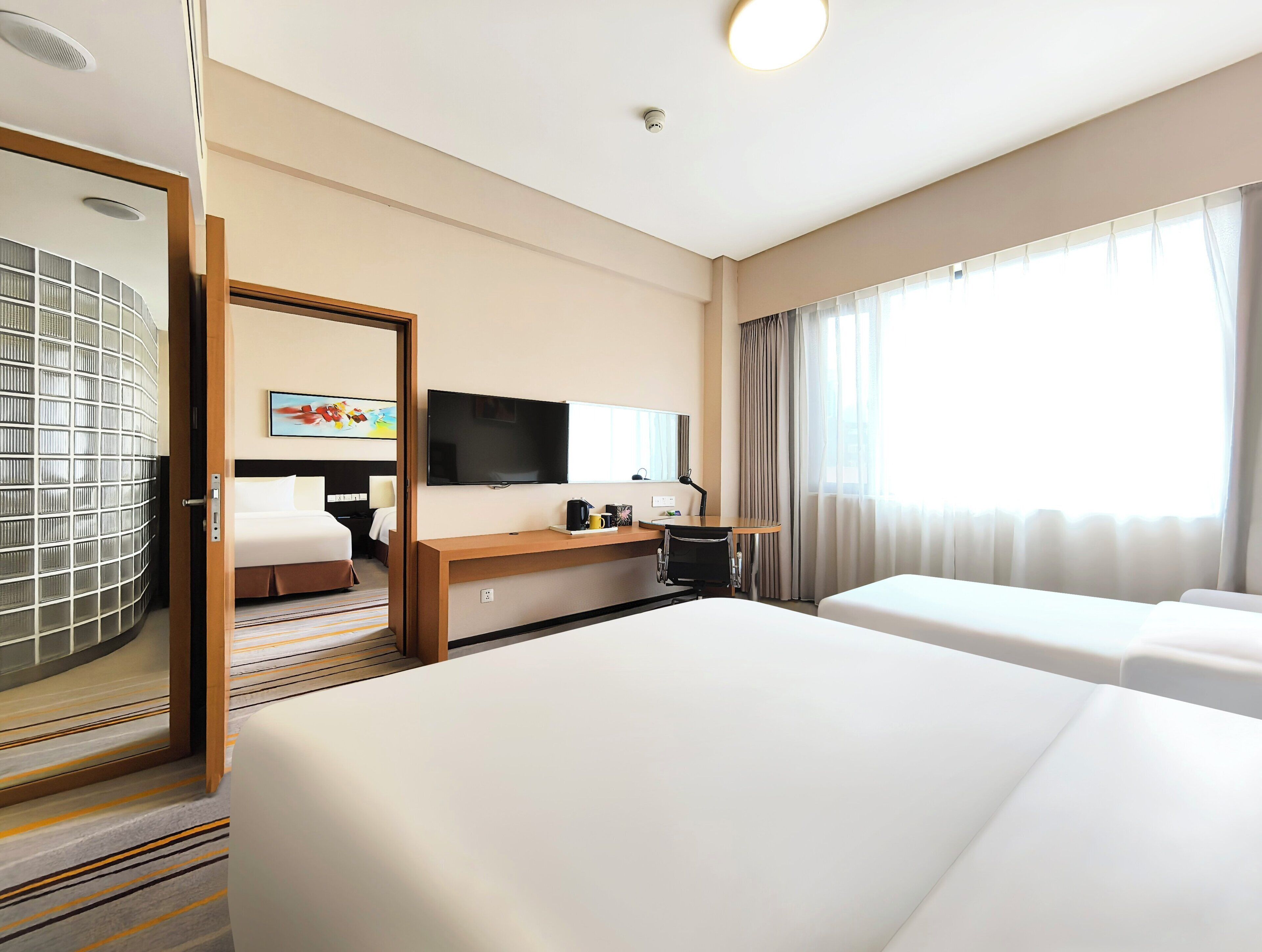 Une chambre d’hôtel avec un lit, un bureau et une chaise, une télévision et une grande fenêtre avec des rideaux.