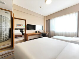 Una habitación de hotel con cama, escritorio y silla, televisor y un amplio ventanal con cortinas.