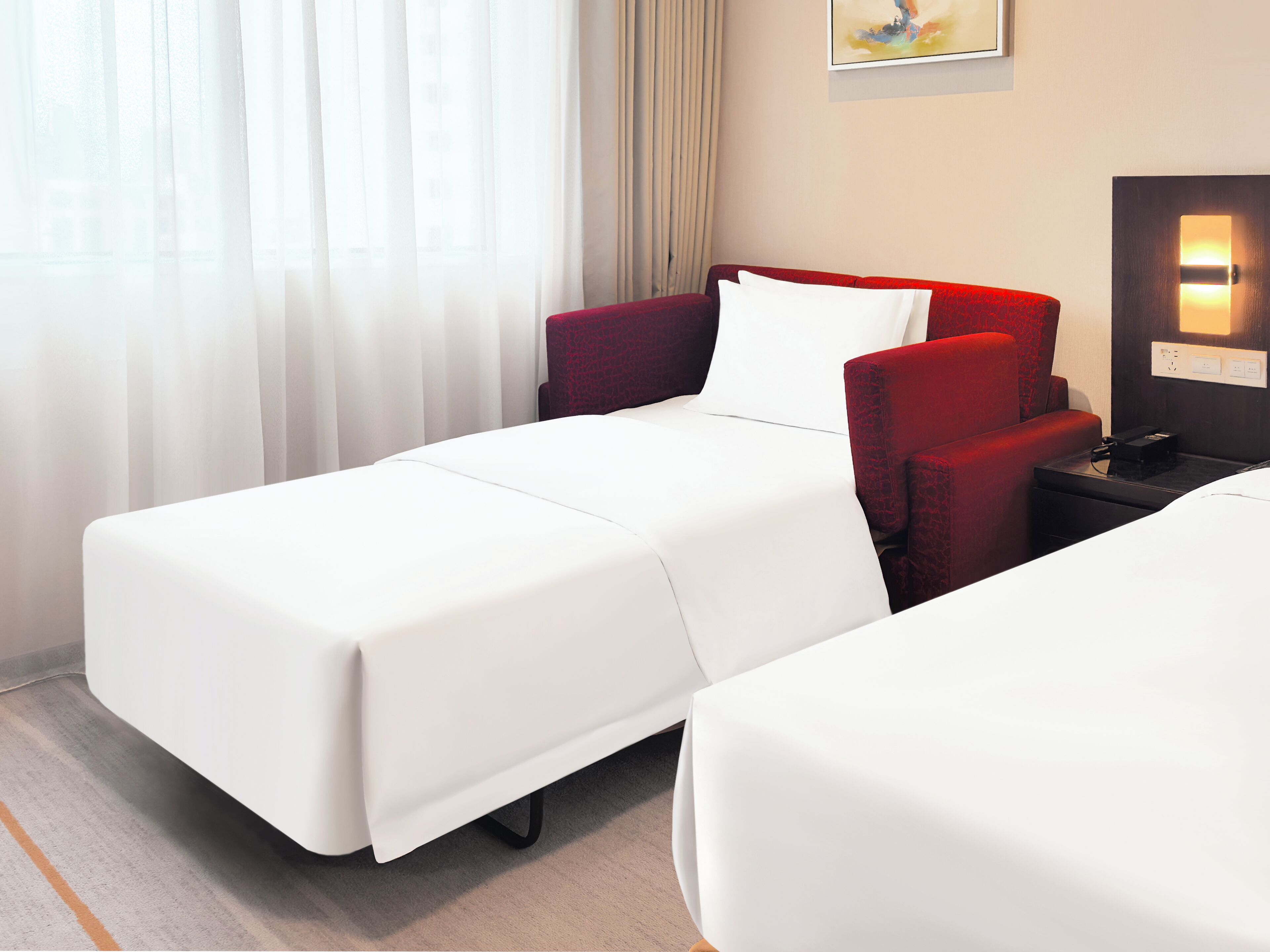 Ein Hotelzimmer mit zwei Betten, einem roten Sessel, einem Nachttisch und einem Bild an der Wand.