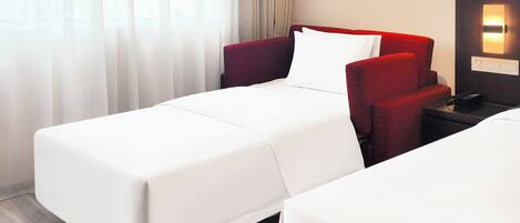Ein Hotelzimmer mit zwei Betten, einem roten Sessel, einem Nachttisch und einem Bild an der Wand.